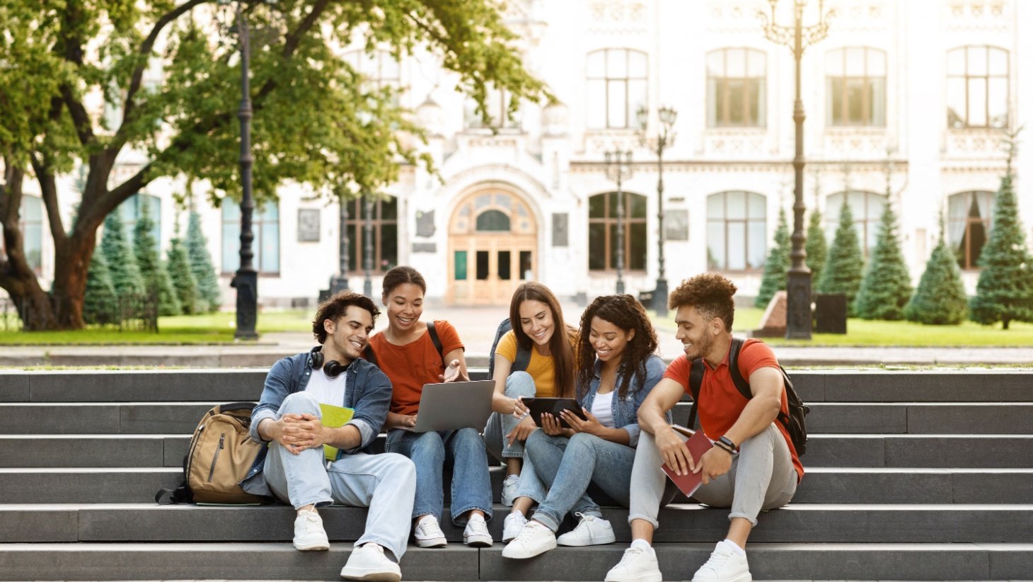 A group of college students sitting together on campus steps, talking and laughing