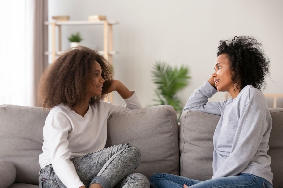 A parent and their child sitting on a couch at home, having a relaxed face-to-face conversation